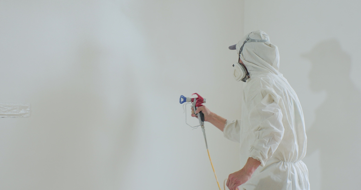 Man in protective gear paint a wall with an airless spray gun. Airless spray painting. Repair of the apartment.